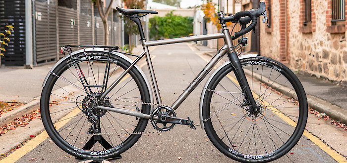 A Bossi Grit titanium bicycle in a custom commuter build, in a quiet city alleyway