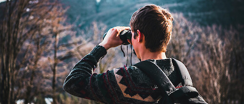 A young man with binoculars, looking out over a forest