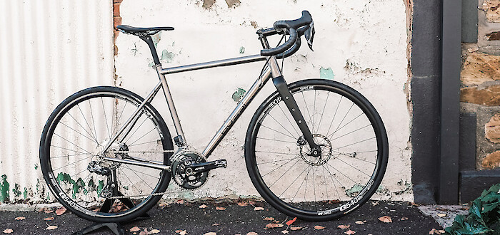 A Bossi Grit SX titanium bike in a custom build, against a white wall with peeling paint